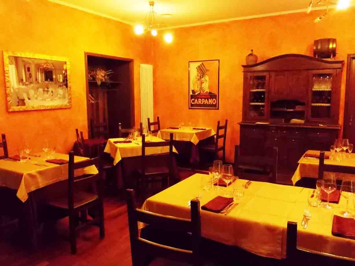 Sala di ristorante con tavole apparecchiate, tovaglie gialle, poster Carpano e credenza in legno