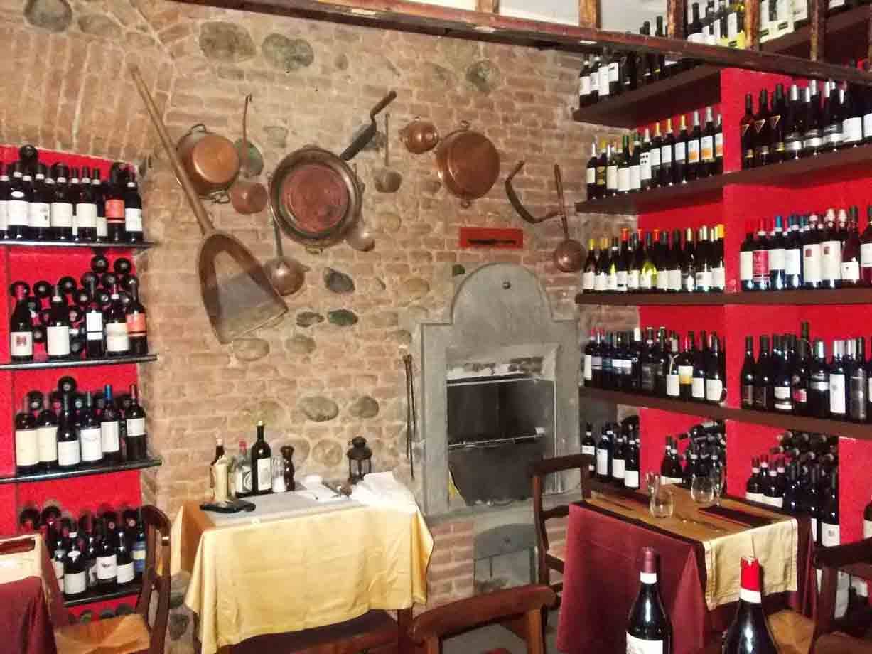 Cantina-ristorante con bottiglie su scaffali rossi, pentole di rame e forno in pietra