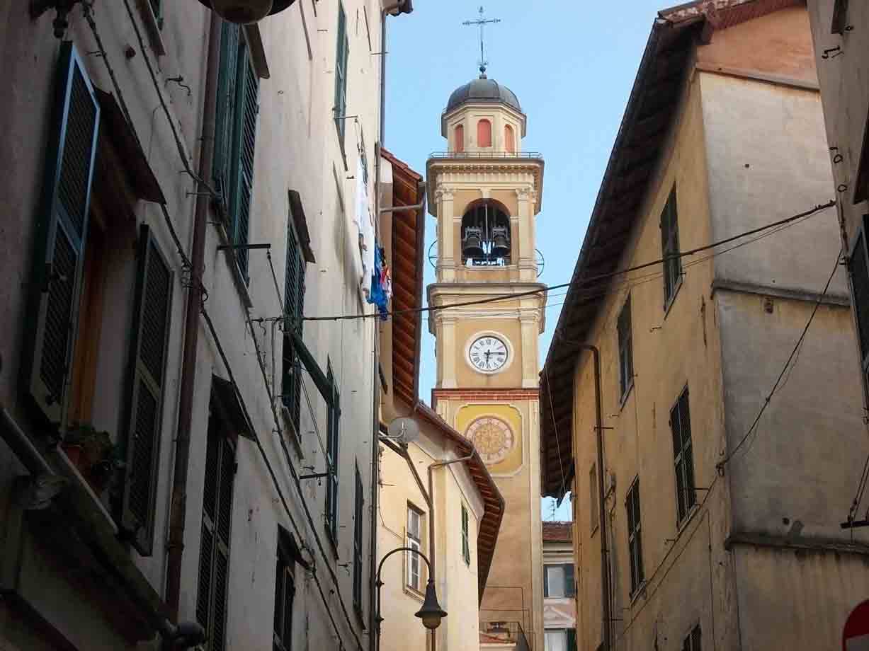 Campanile con orologio tra case color ocra e tapparelle verdi
