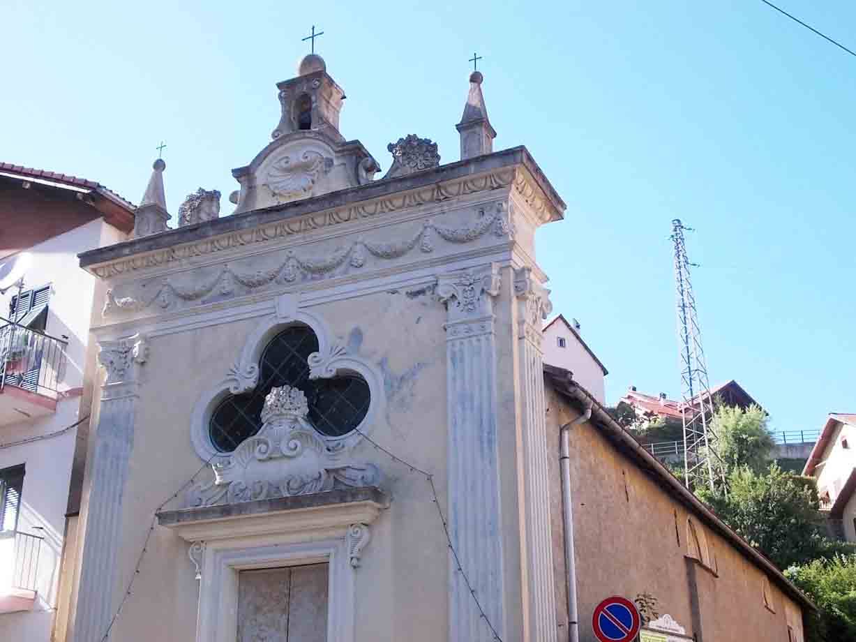 Facciata barocca di cappella con finestra quadrilobata, intonaco chiaro, cielo azzurro