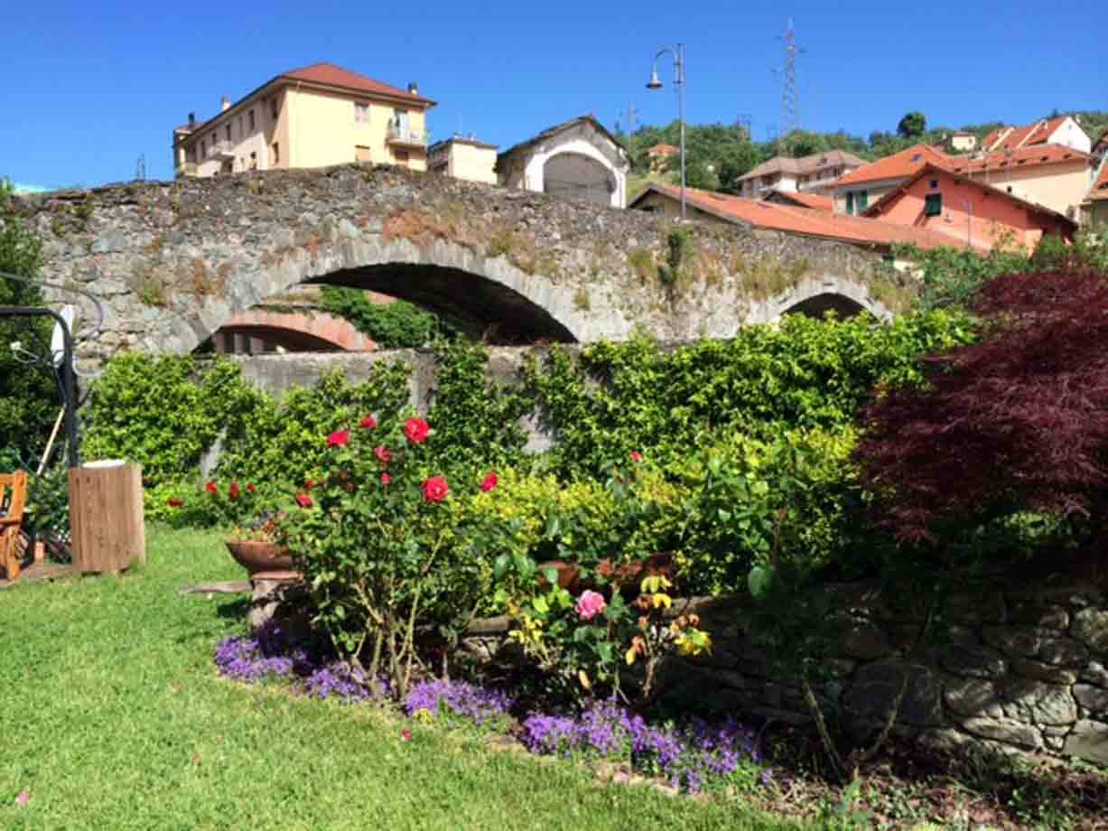 Antico ponte in pietra con archi sopra un giardino fiorito di rose