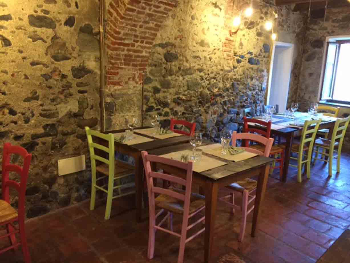Sala rustica con pareti in pietra, tavoli apparecchiati e sedie colorate