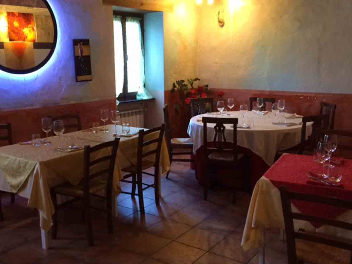 Sala di trattoria con tavoli apparecchiati, tovaglie colorate, sedie di legno e luce calda