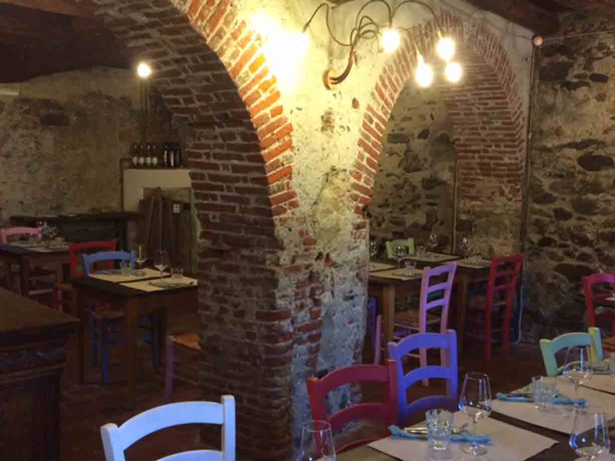 Trattoria rustica con volte in mattoni, sedie colorate e tavoli apparecchiati a luce calda