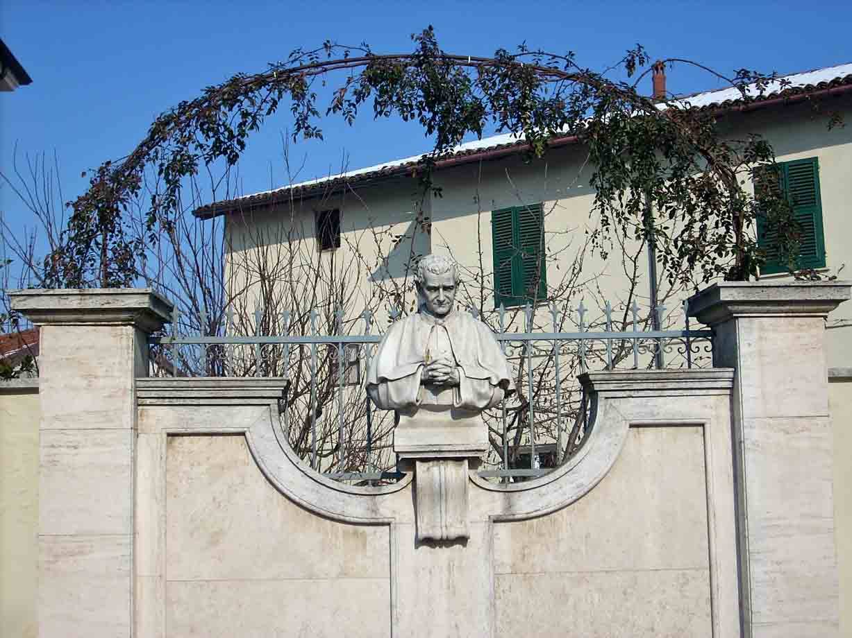 Busto marmoreo di ecclesiastico su cancello in pietra davanti a casa con persiane verdi