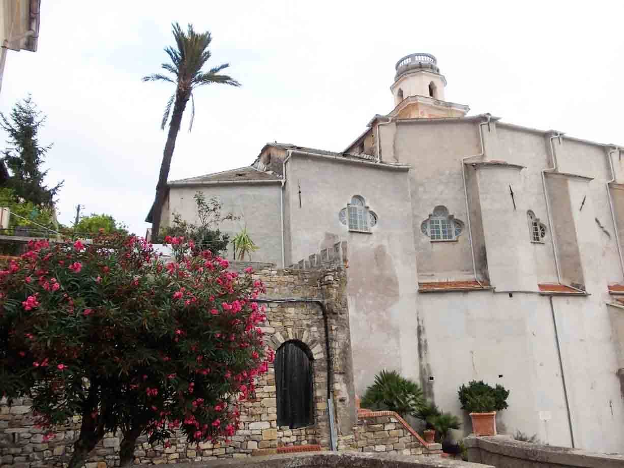 Chiesa bianca con campanile, oleandro fiorito e palma, mura in pietra