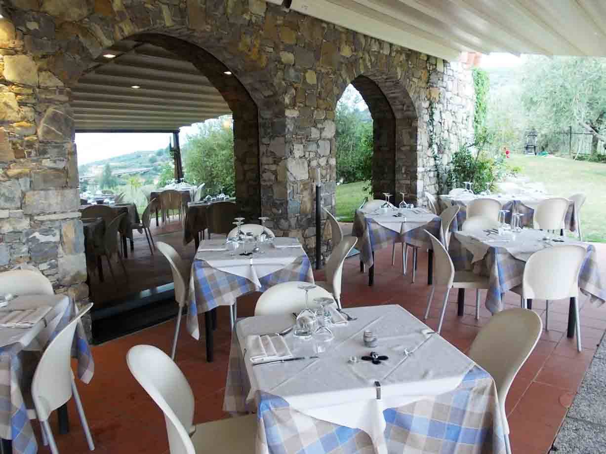 Terrazza di ristorante con tavoli apparecchiati, pareti in pietra, archi e sedie bianche
