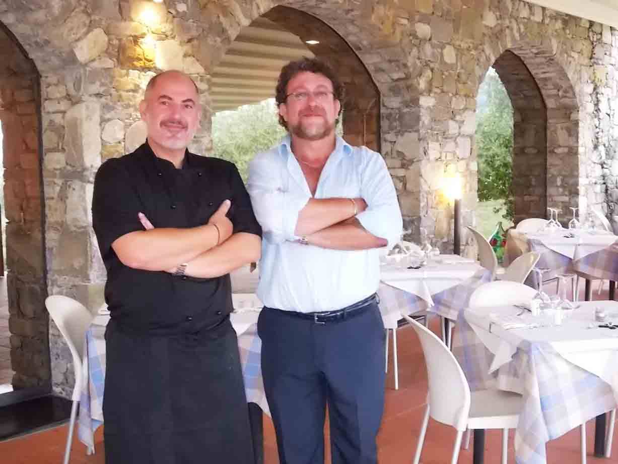 Due uomini con braccia incrociate in ristorante con arcate in pietra e tavole apparecchiate