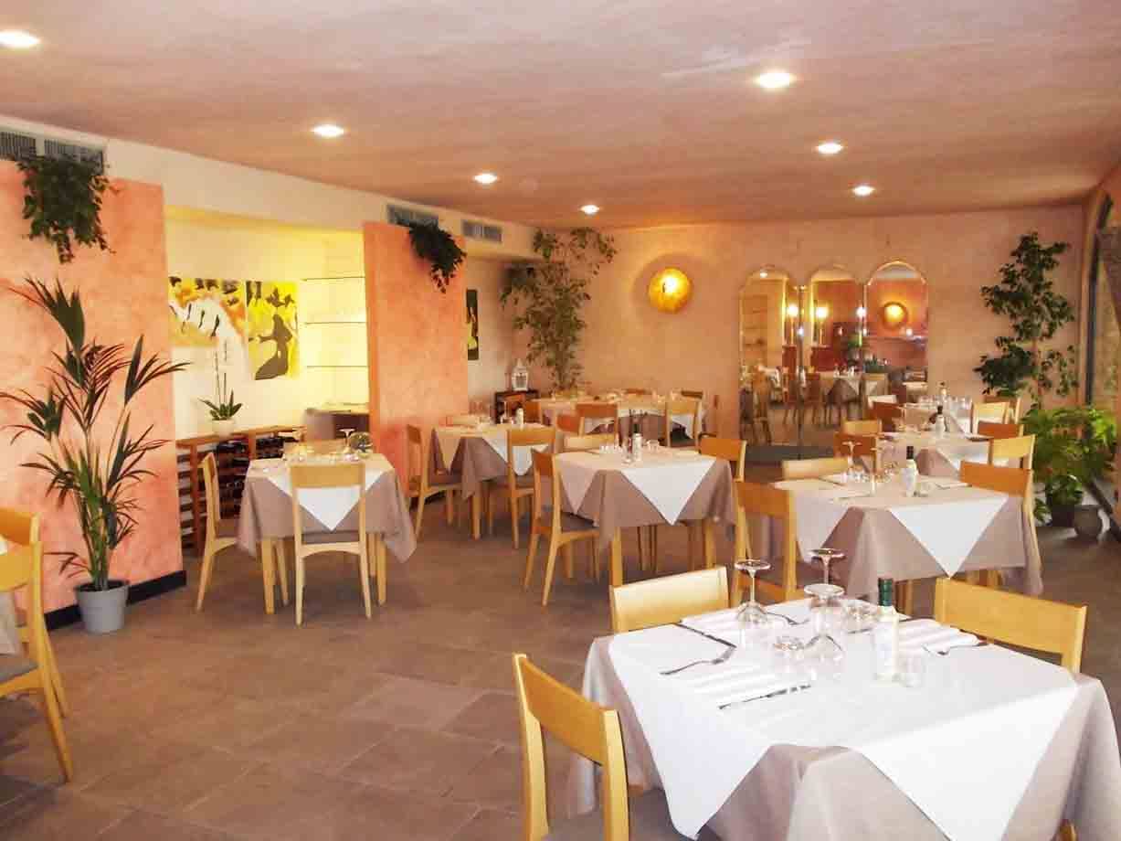 Sala di ristorante con tavoli apparecchiati a tovaglia bianca, pareti rosa e piante