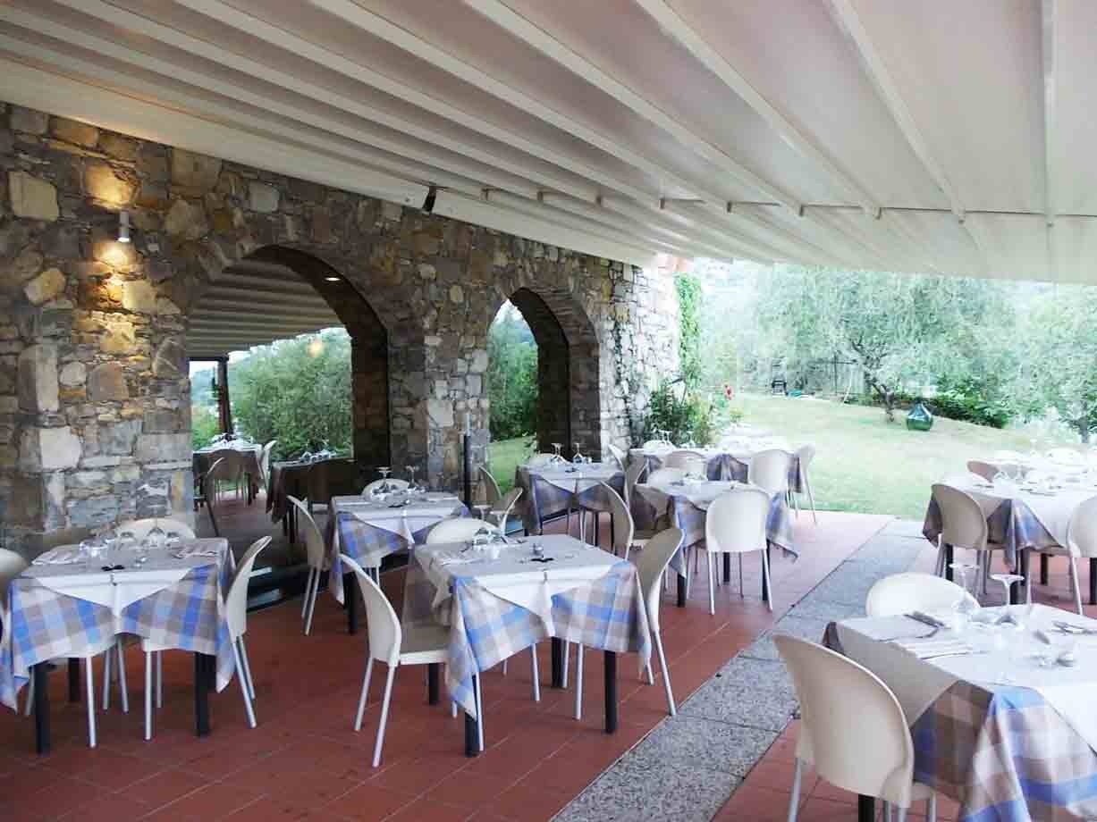 Terrazza di ristorante con tavoli apparecchiati, tovaglie a quadri e archi in pietra