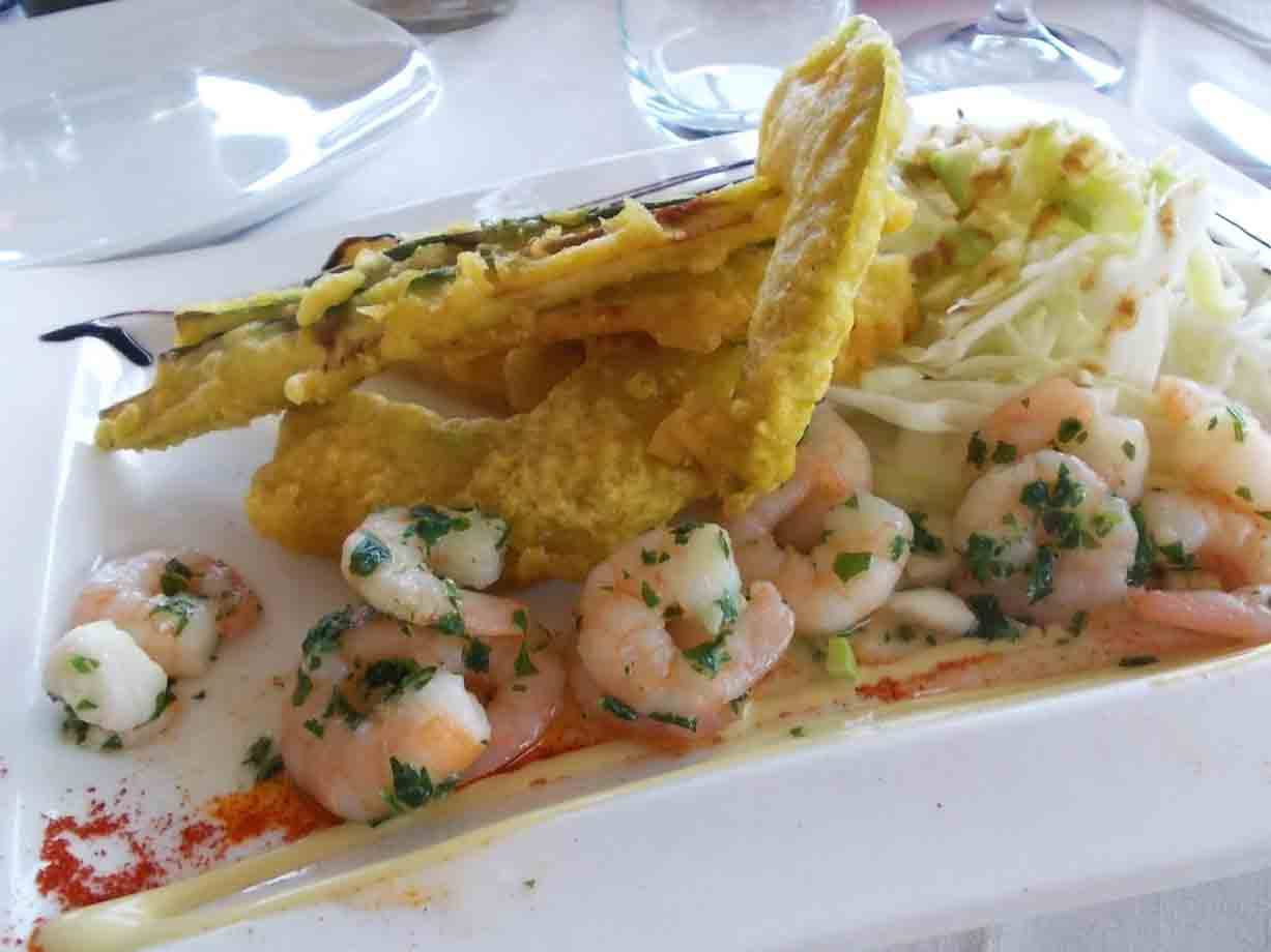 Gamberetti alle erbe con frittura croccante e insalata su piatto bianco