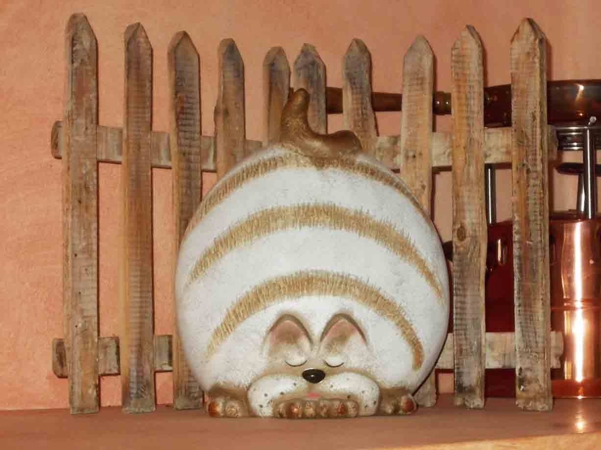 Statua ceramica di gatto addormentato davanti a una staccionata di legno