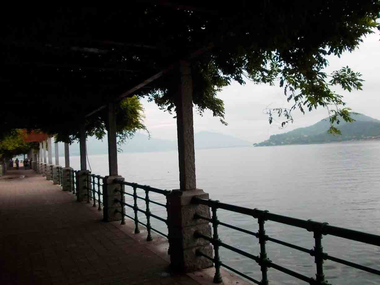 Passeggiata coperta con pilastri di pietra e ringhiera verde sul lago