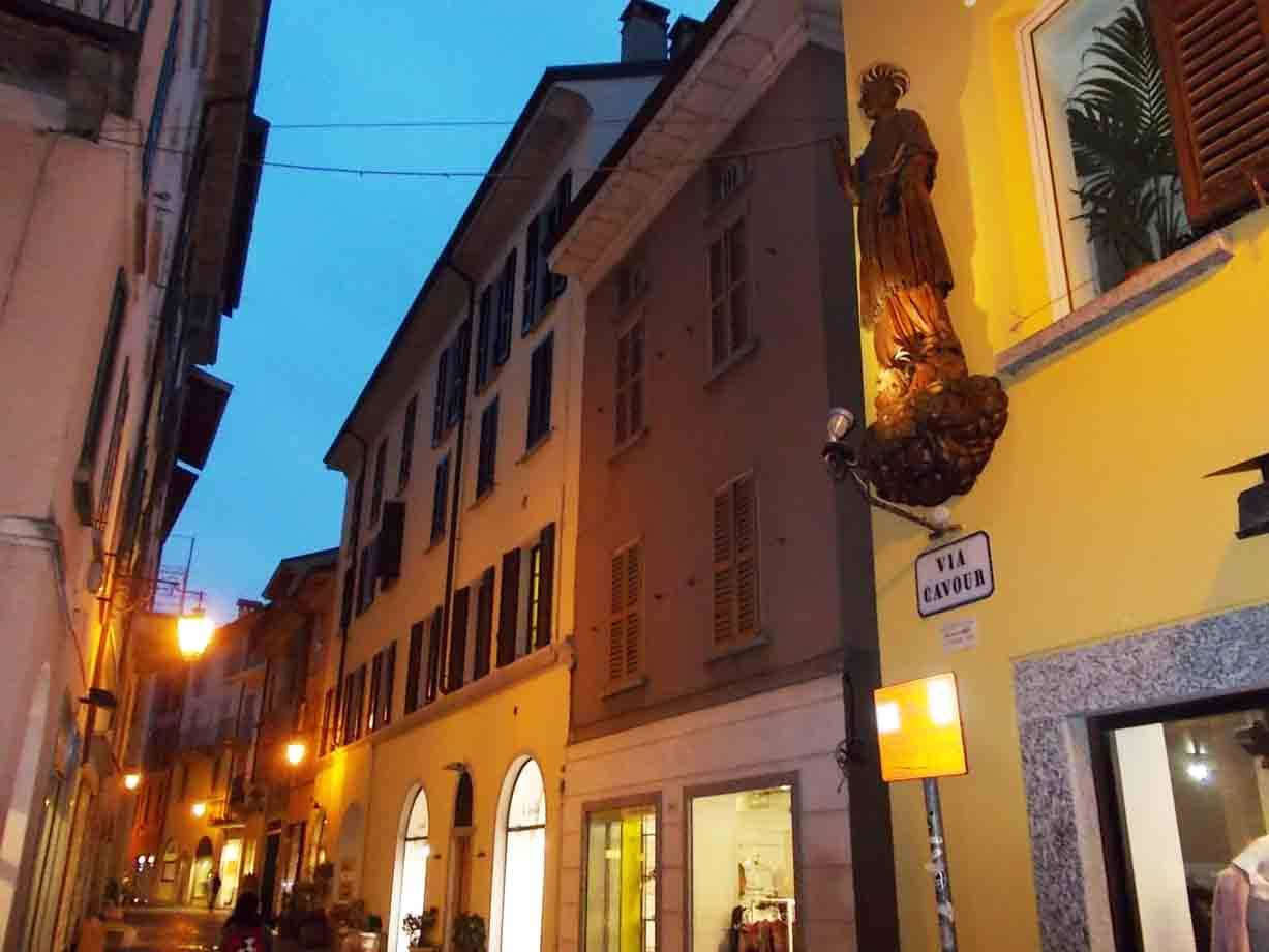 Statua lignea illuminata sulla facciata gialla di Via Cavour al crepuscolo