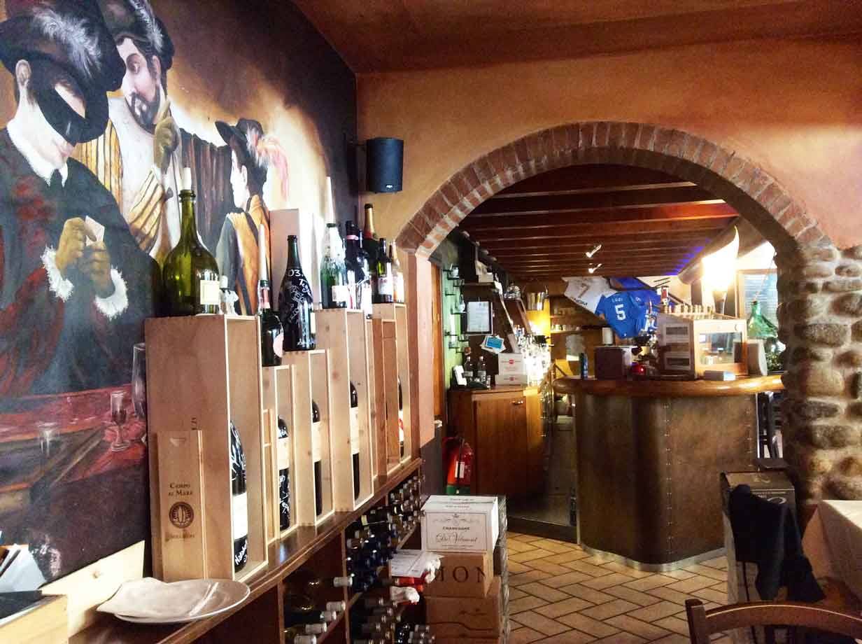Bottiglie di vino in cassette di legno sotto un affresco, arco di mattoni verso il bancone