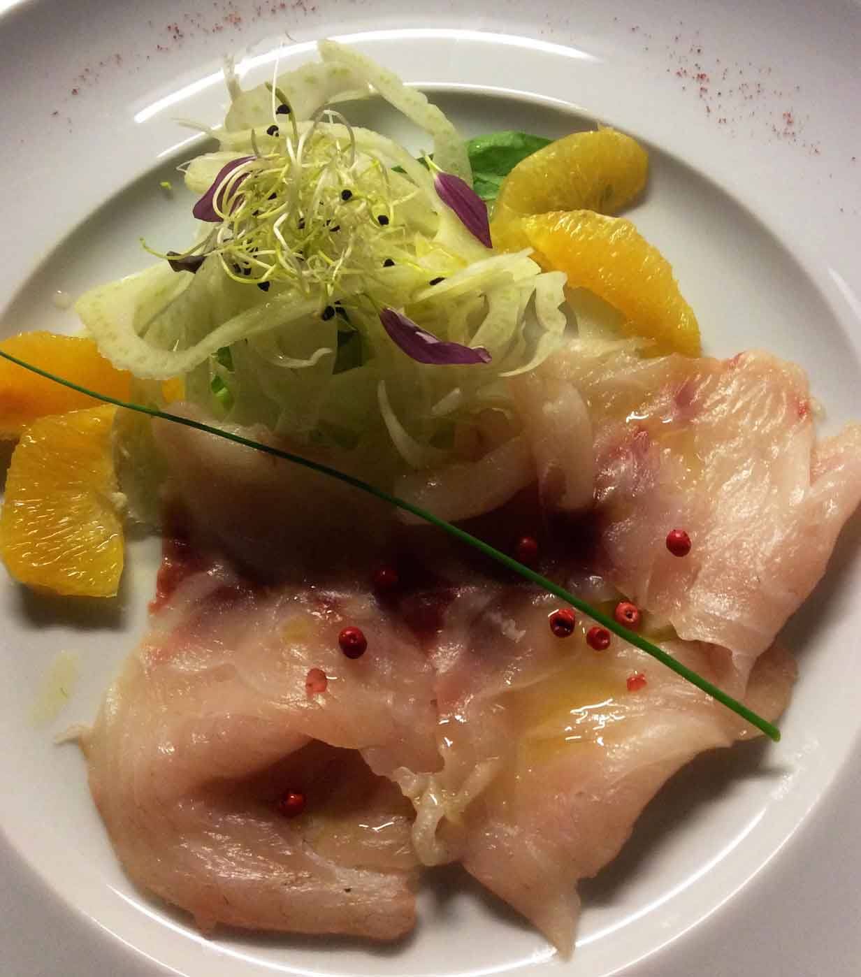 Carpaccio di pesce crudo con arance, finocchi e germogli su piatto bianco