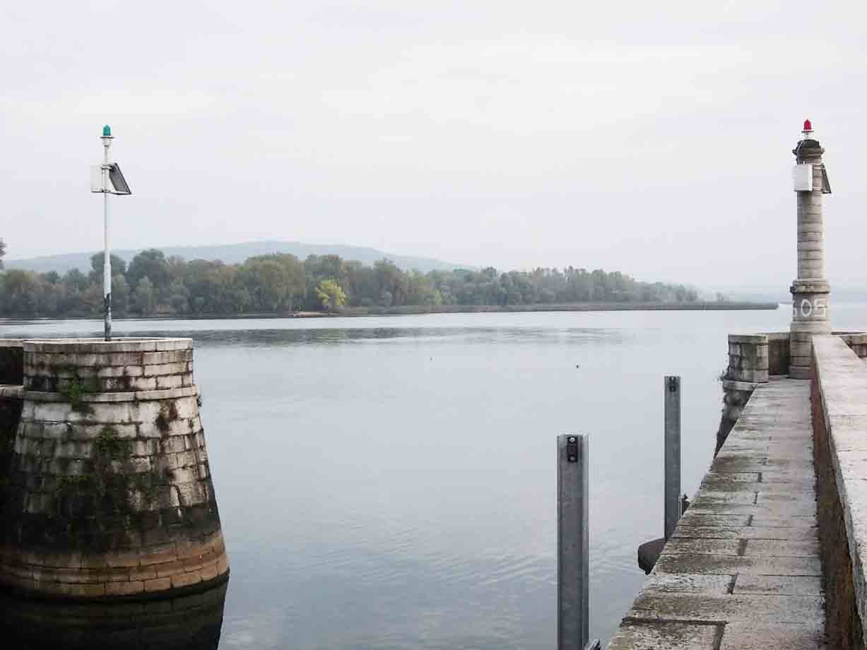 Diga in pietra con faro segnaletico sul lago, luci rosse e verdi, giorno nuvoloso