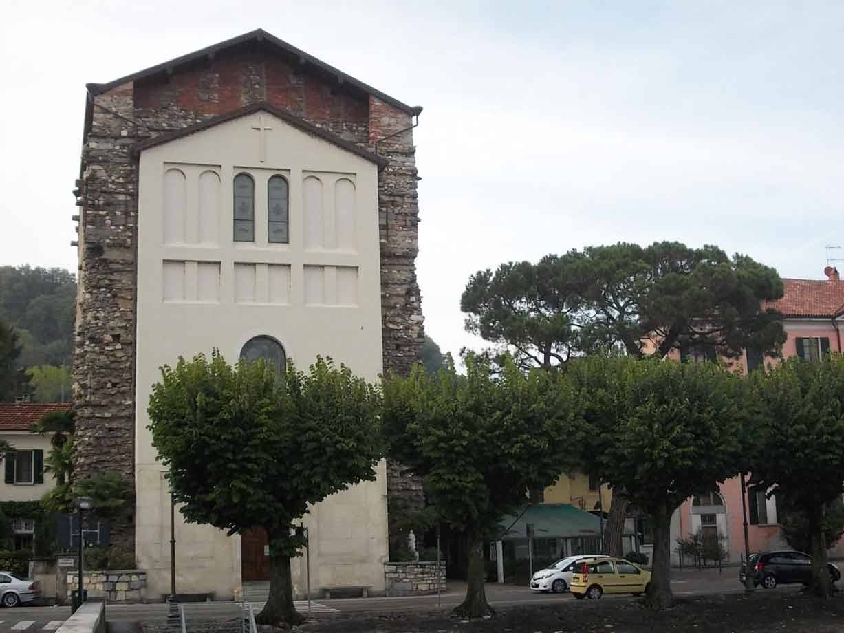 Chiesa in pietra e intonaco bianco con facciata, alberi e auto in piazza