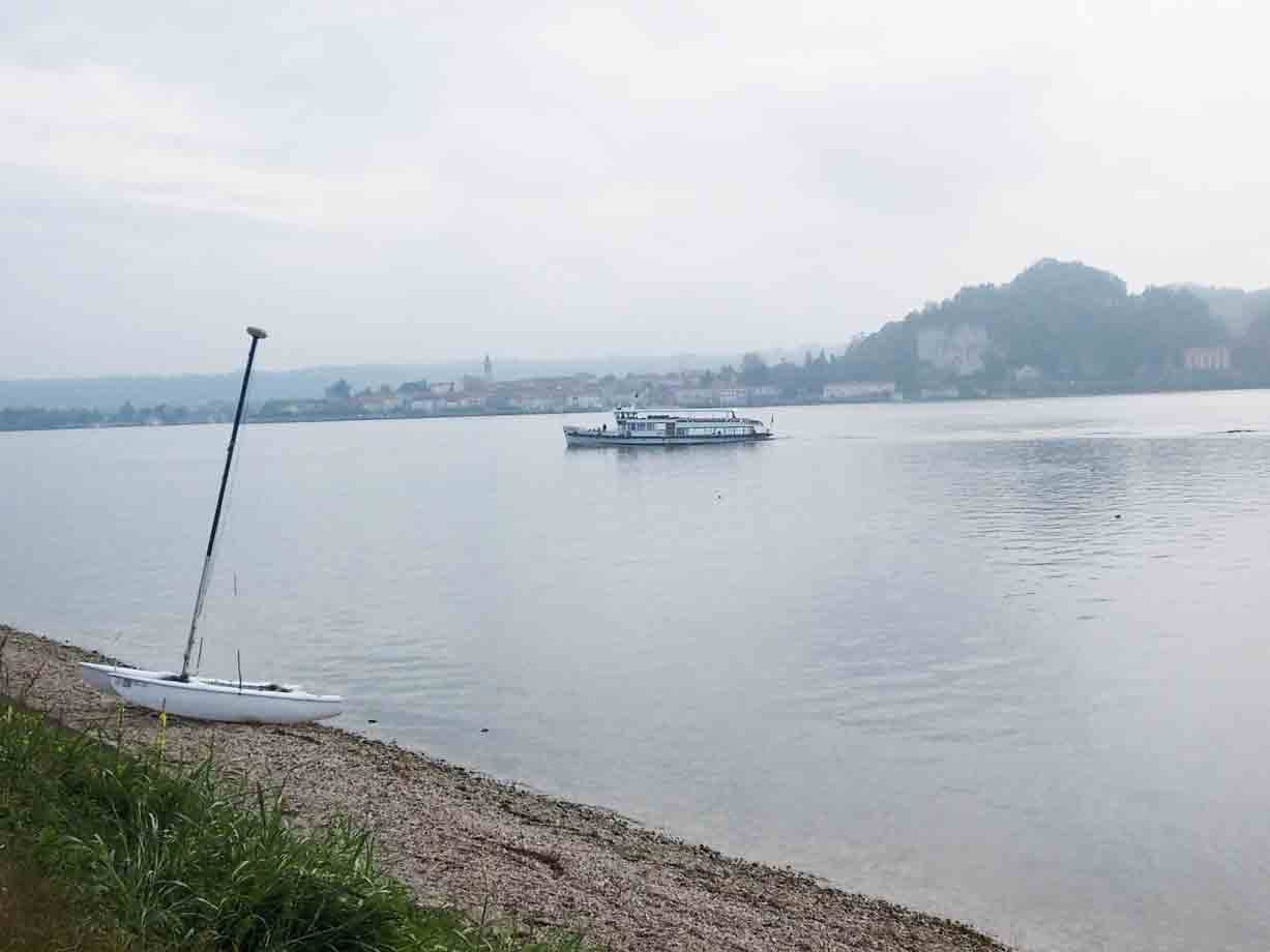 Traghetto sul lago nebbioso, piccola barca a vela arenata sulla spiaggia ghiaiosa