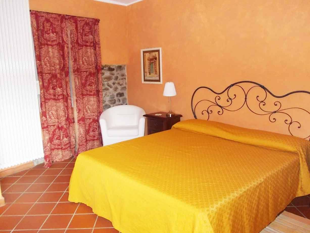 Camera con letto matrimoniale coperto di giallo, testiera in ferro battuto, pareti arancioni