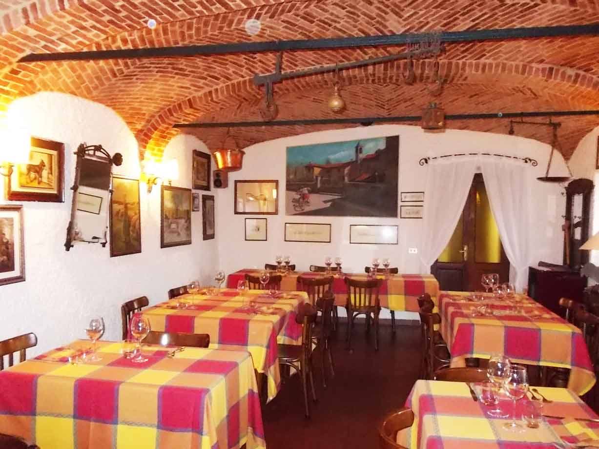Sala di trattoria con volte in mattoni, tavole apparecchiate a tovaglie scozzesi gialle e rosse
