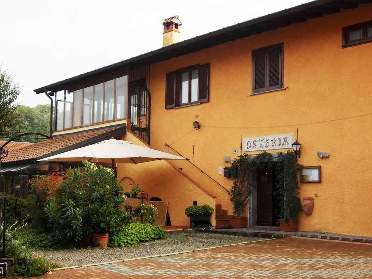 Facciata ocra dell'osteria con ombrellone, piante in vaso e ingresso verdeggiante