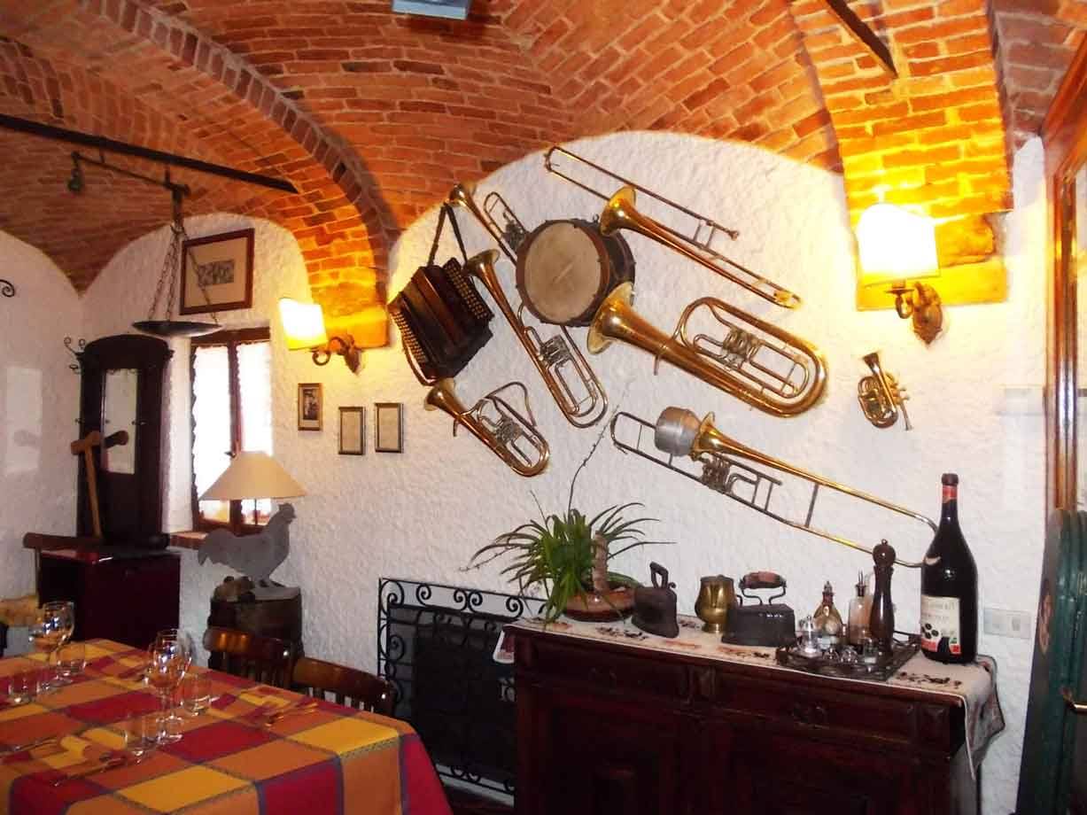 Sala di trattoria con volta in mattoni, strumenti musicali d'ottone appesi al muro bianco