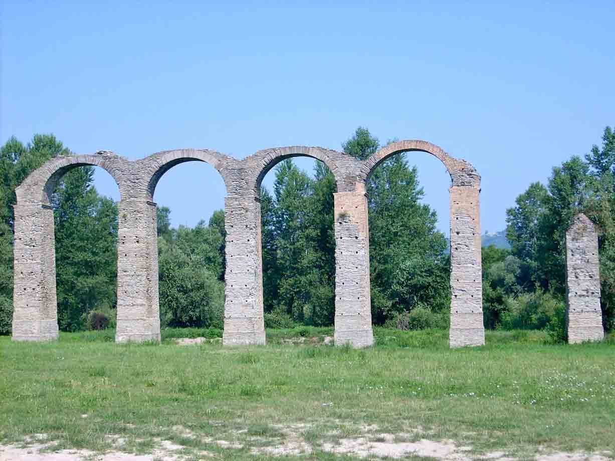 Antichi archi di acquedotto romano in pietra tra prato verde e alberi