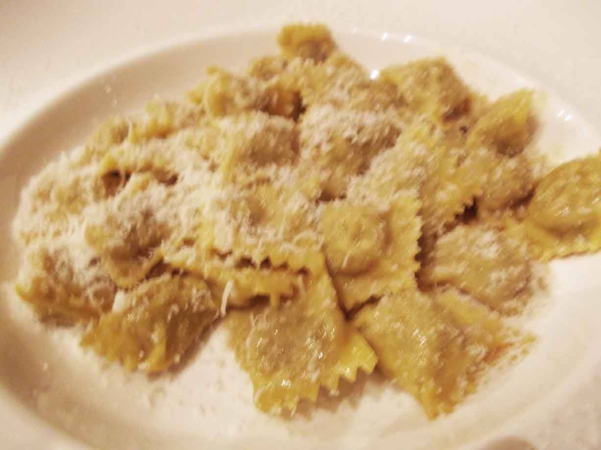 Piattino bianco con ravioli di carne conditi e grattugiata abbondante, luce calda