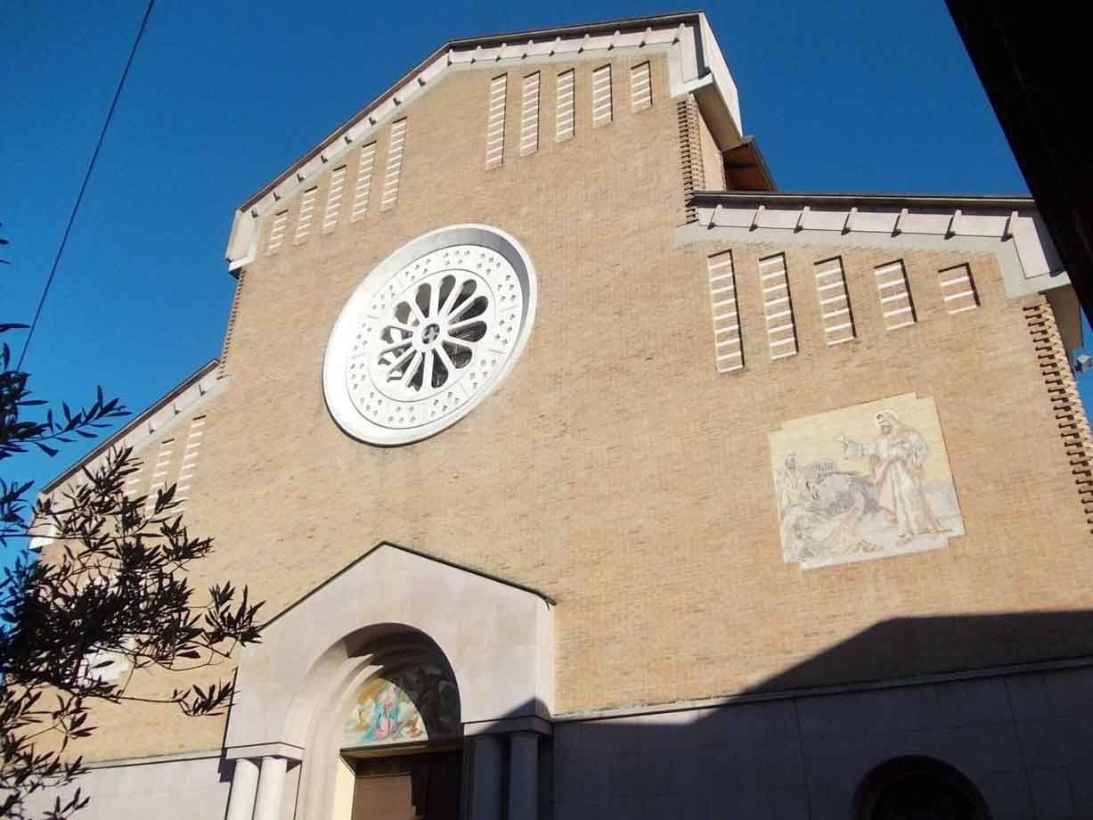 Facciata in mattoni di una chiesa con rosone bianco e affresco, rami in controluce