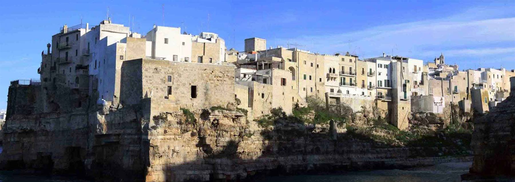 Case bianche e bastioni di pietra sopra la scogliera a Polignano a Mare
