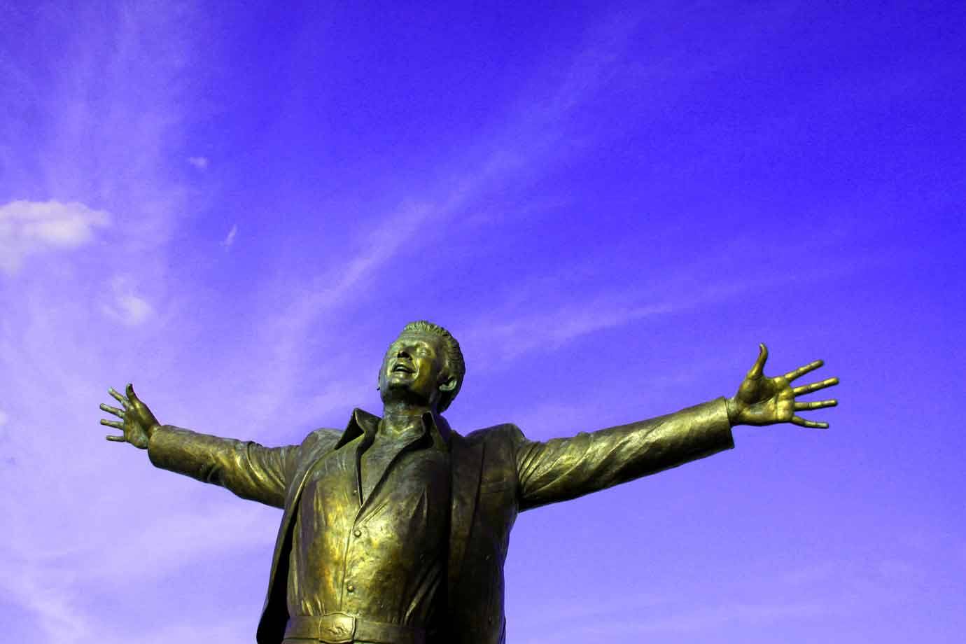 Statua in bronzo a braccia aperte verso il cielo azzurro