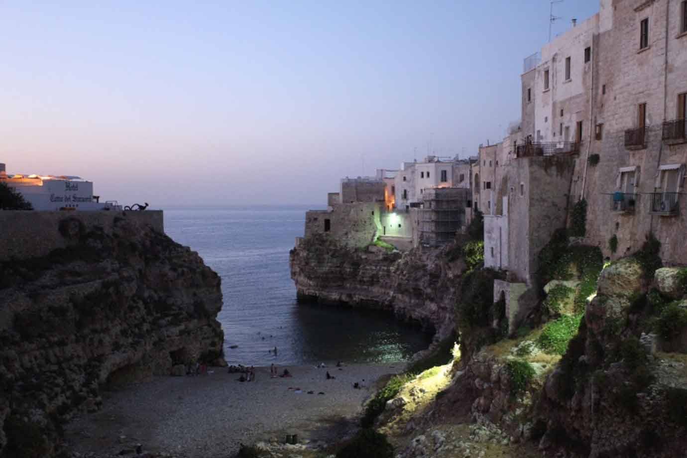 Polignano a Mare, case bianche sulla scogliera e spiaggia sotto cielo serale