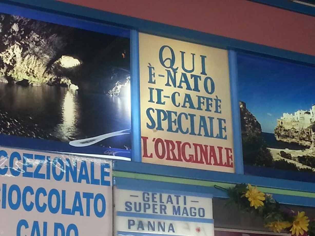 Insegna 'Qui è nato il caffè speciale' con foto di grotta e paese