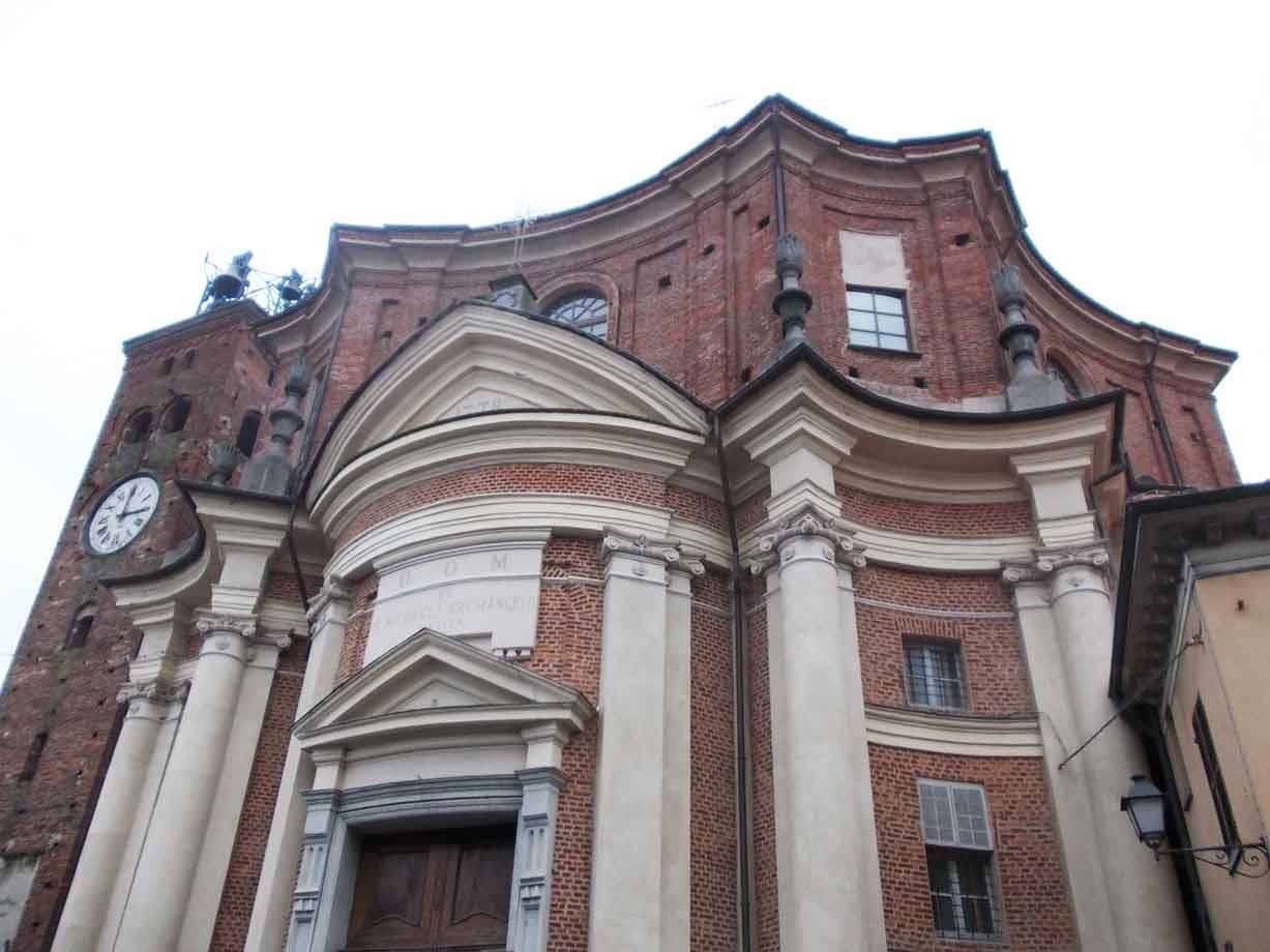 Chiesa barocca in mattoni con facciata curva, colonne chiare e campanile con orologio