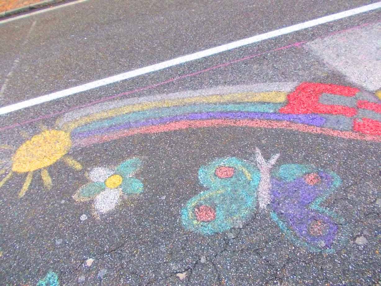 Disegni con gessetti colorati su asfalto: sole, fiore, farfalla e arcobaleno