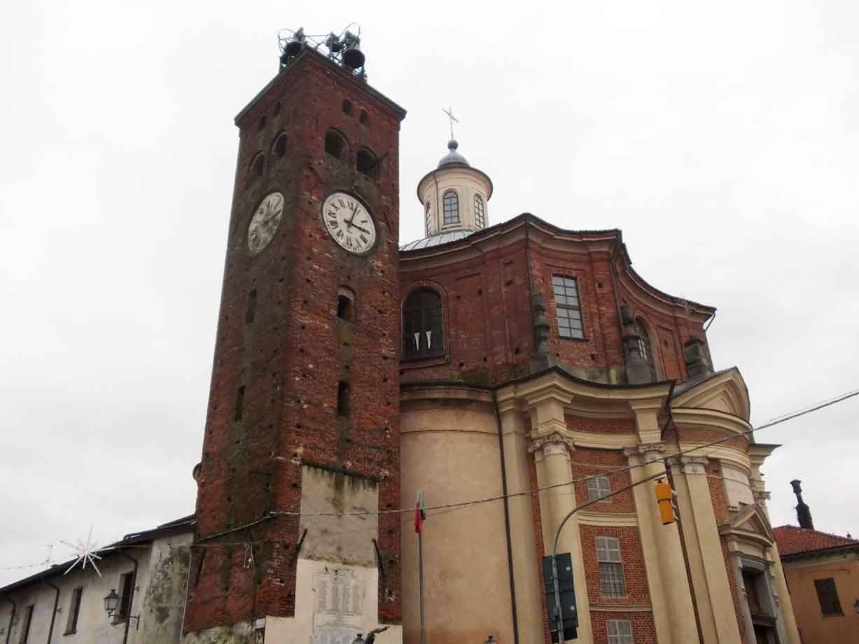 Torre civica in mattoni con orologio accanto alla chiesa barocca, cielo grigio