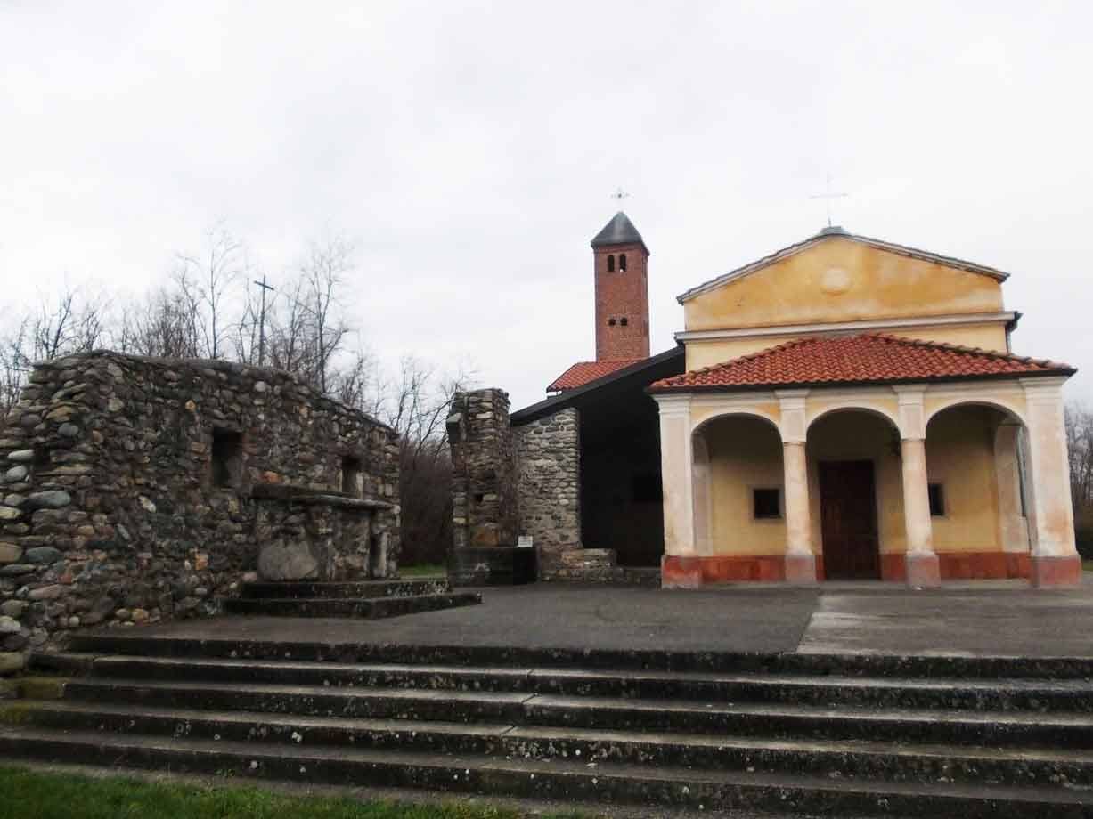 Chiesa con portico ad archi e campanile in mattoni accanto a ruderi di pietra