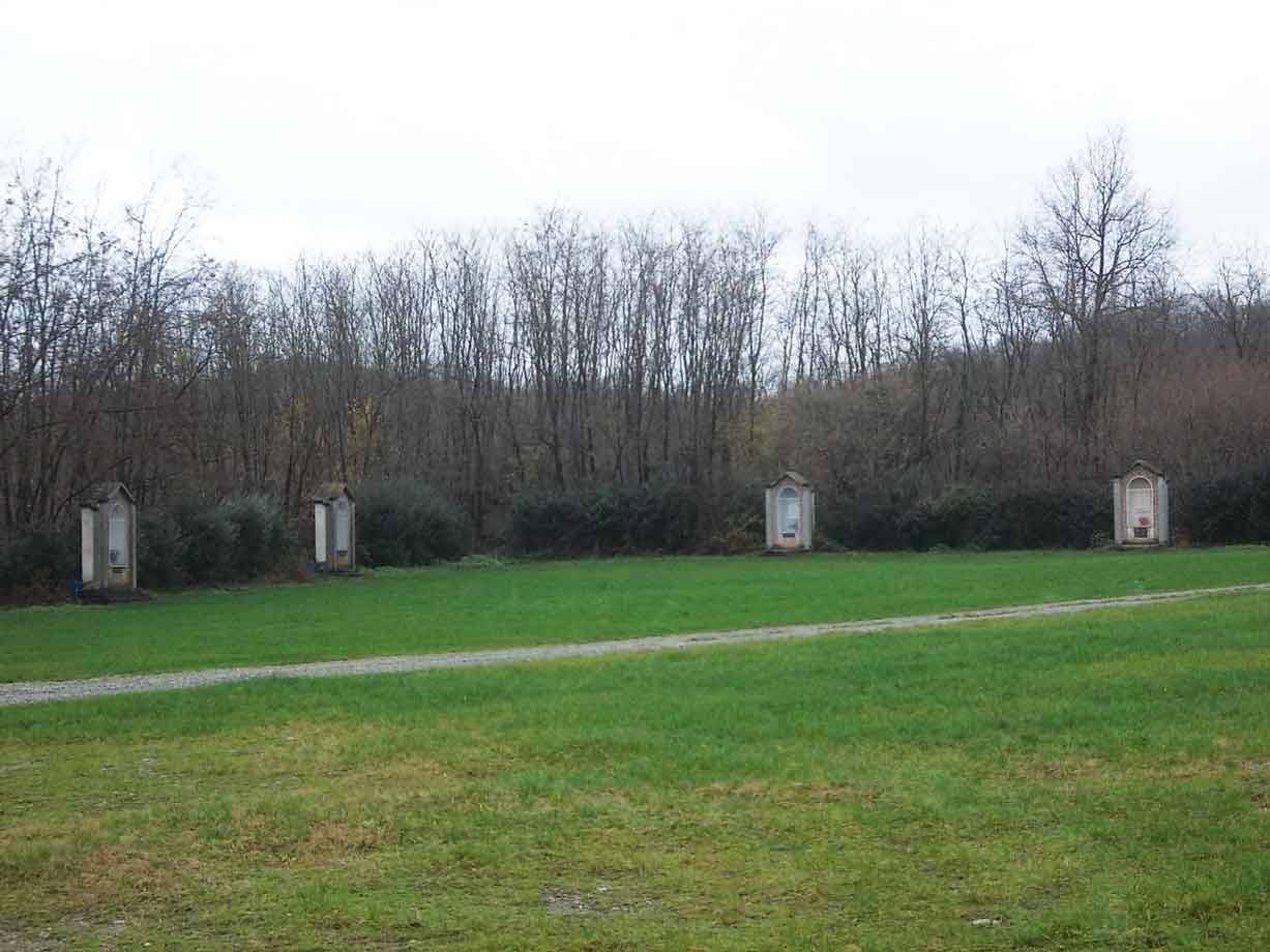 Edicole in pietra allineate sul prato davanti a bosco spoglio