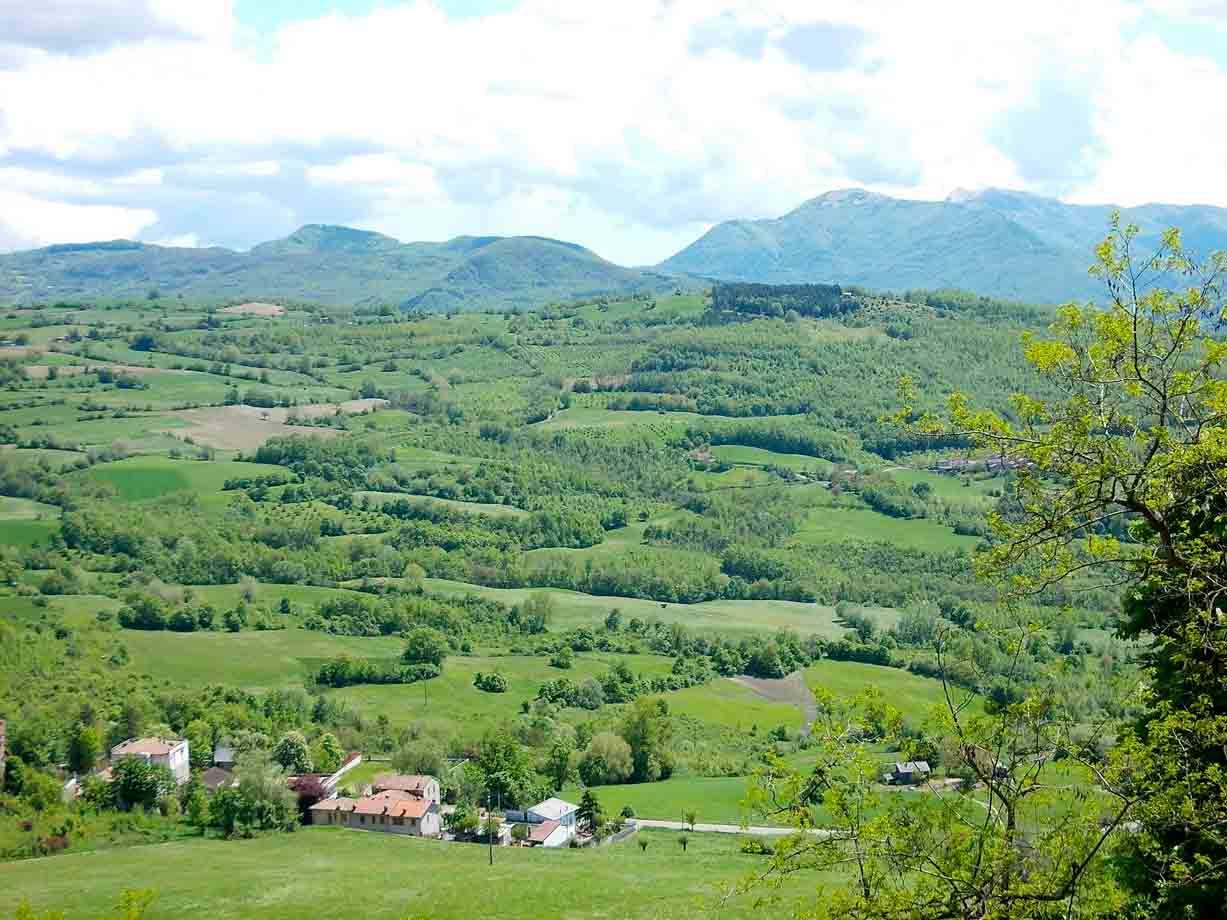 colline verdi con case rustiche e monti sotto nuvole