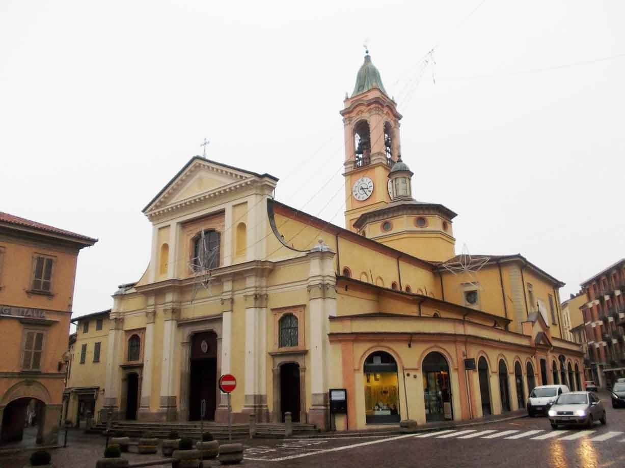 Chiesa gialla con campanile e orologio su strada bagnata, auto in transito