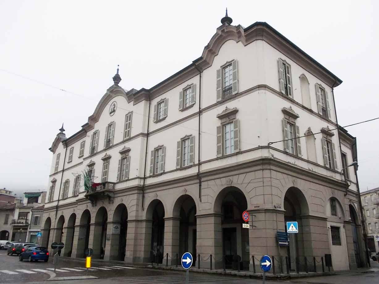 Palazzo bianco con portici ad archi in pietra e finestre con persiane, cielo grigio