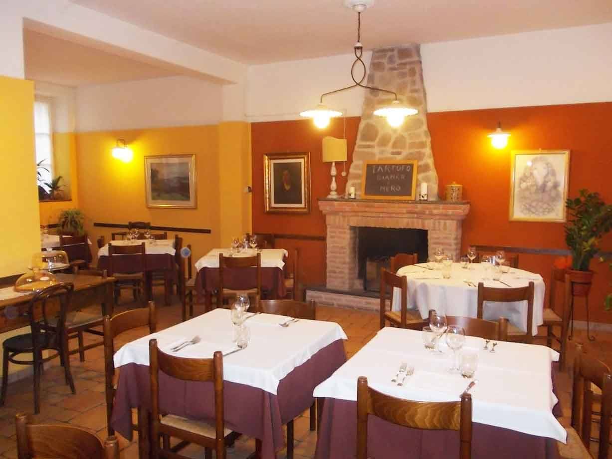 Sala di trattoria con tavoli apparecchiati a tovaglia bianca e camino in mattoni