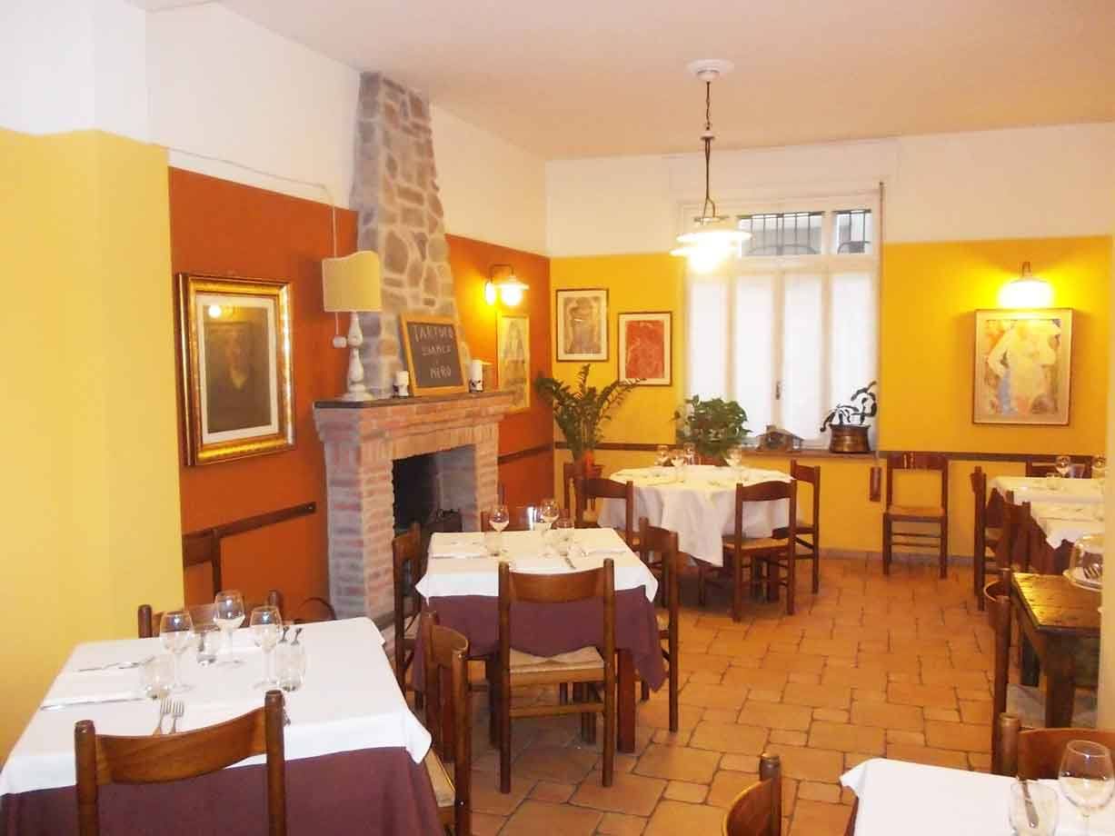 Sala di trattoria con tavoli apparecchiati, camino in pietra e pareti gialle