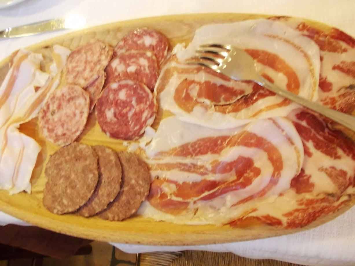 Tagliere di salame, pancetta e coppa su vassoio di legno con forchetta