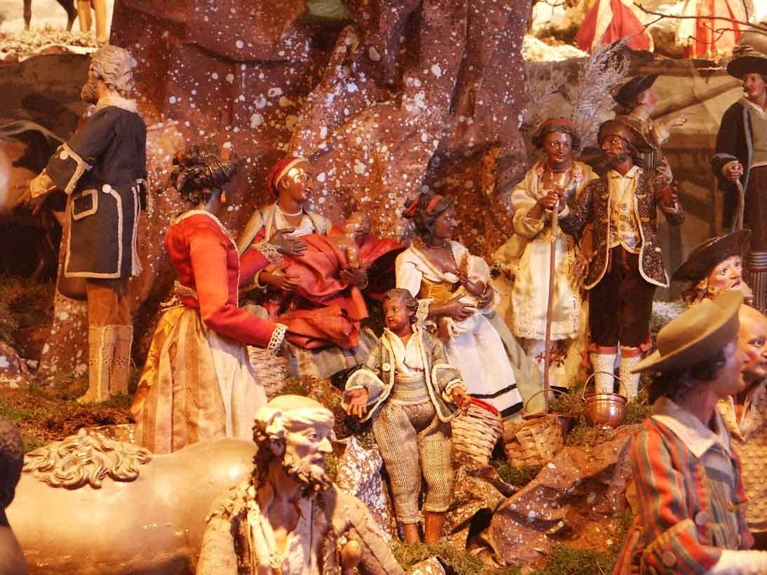 Presepe napoletano con statuine terracotta in abiti settecenteschi sotto luci calde