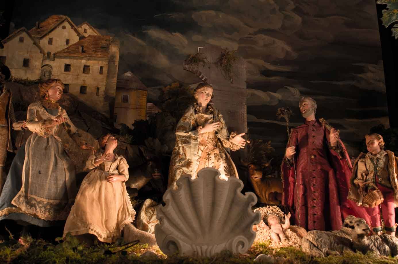 Presepe con statue in stoffa intorno al Bambino Gesù, sotto un cielo dipinto