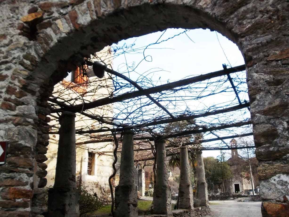 Arco in pietra con pergolato di tralicci legnosi e colonne, borgo sullo sfondo