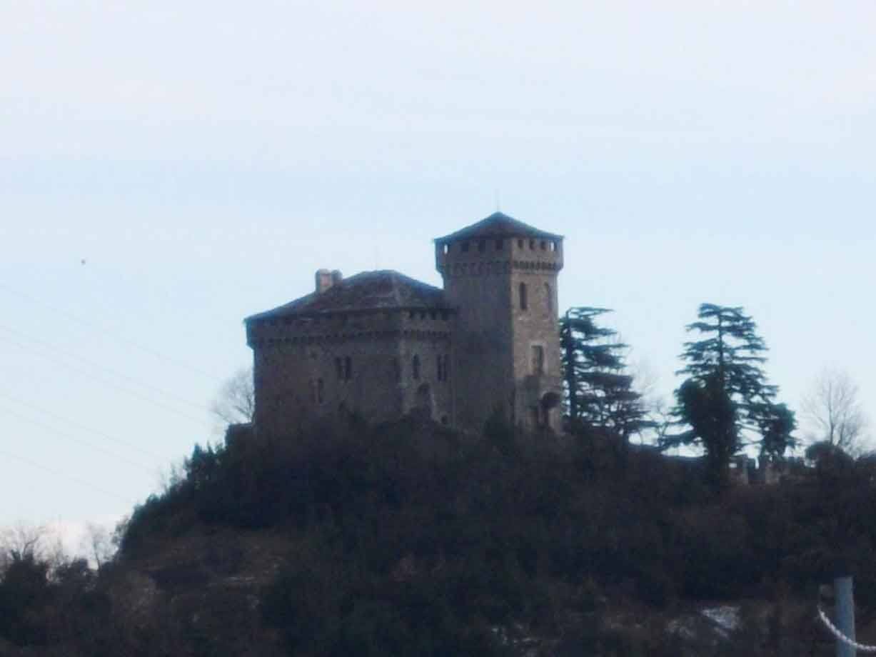 Castello in pietra con torre merlata sulla collina boscosa, cielo grigio