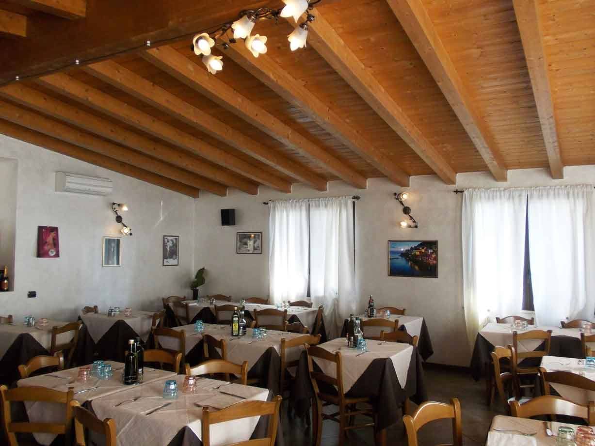 Sala ristorante con tavoli apparecchiati, soffitto in travi di legno e luce naturale